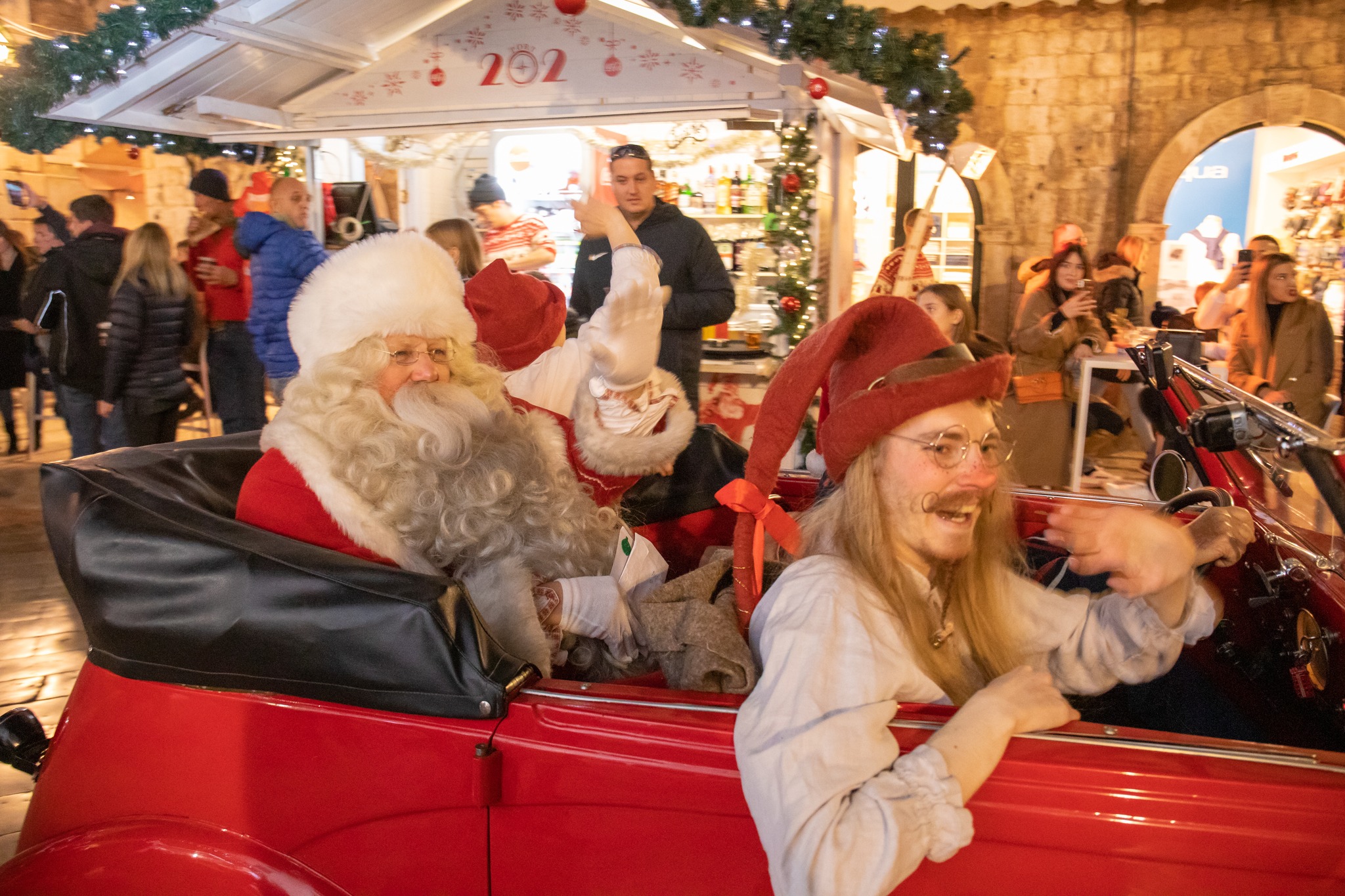 Santa Claus and an elf waving from a red vintage car at the Dubrovnik Winter Festival