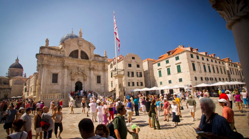 Crowds of visitors on Luža Square in front of St Blaise's Church and the flag on Orlando's Column