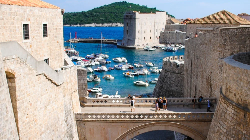 Boats in Dubrovnik's old harbour seen from the city walls, with a stone fortress and Lokrum island behind