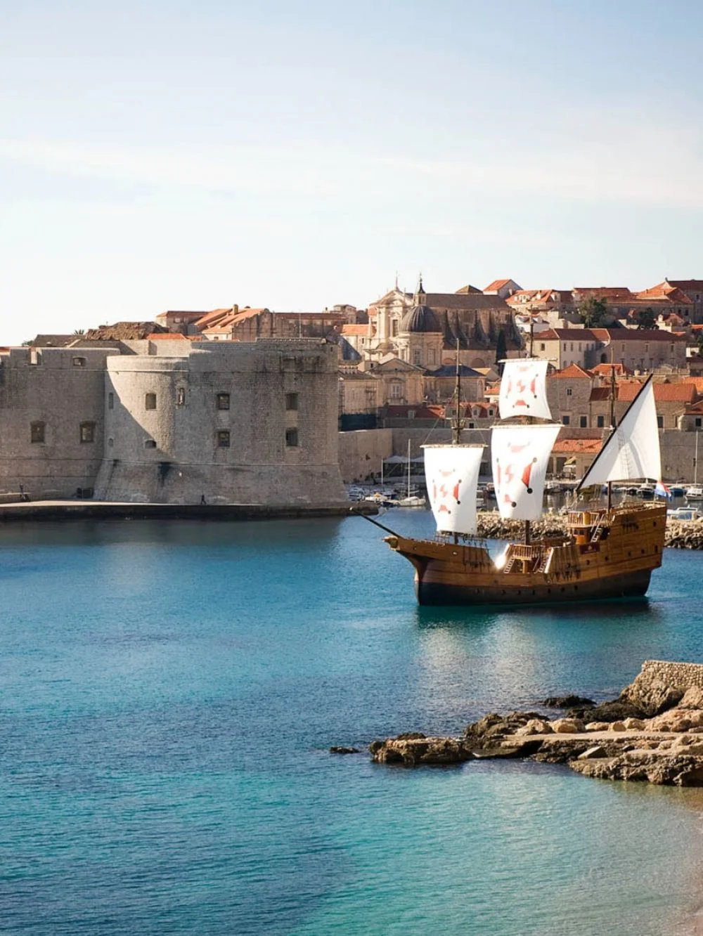 Wooden sailing ship with white sails in Dubrovnik's harbour below St John's Fortress and the Old City