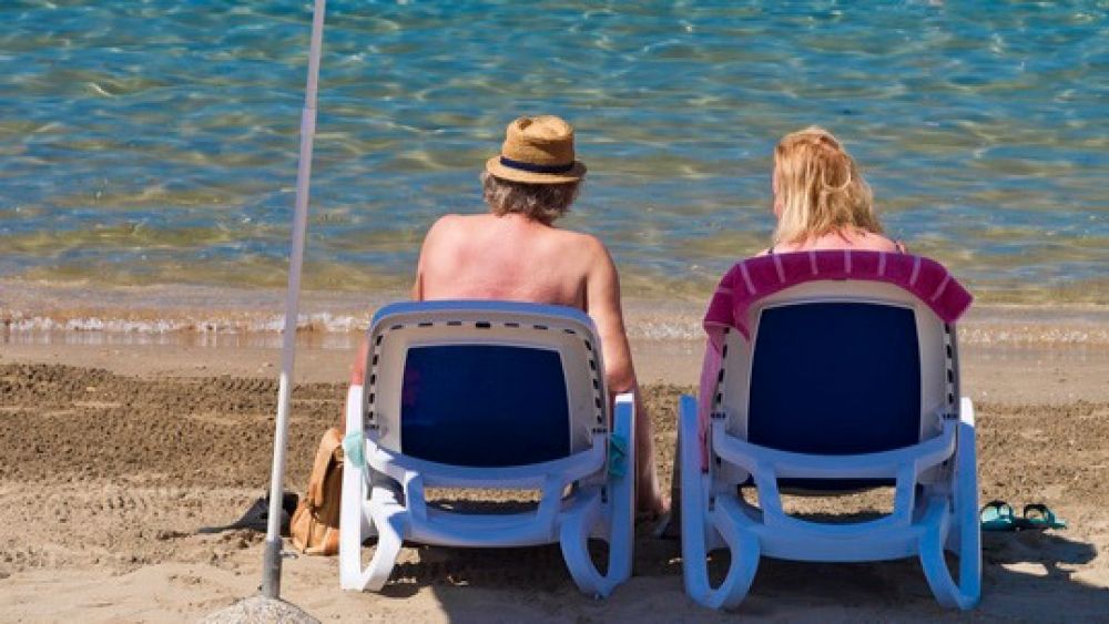 Two people relaxing on white sun loungers on a sandy beach by clear water
